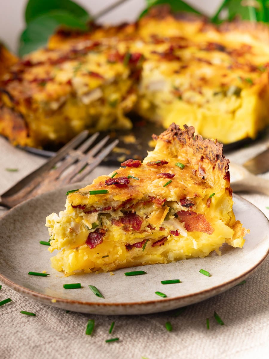 Slice of Potato Crust Quiche on a plate with fork, topped with chives.