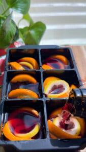 Orange slices and red wine in ice cube tray.