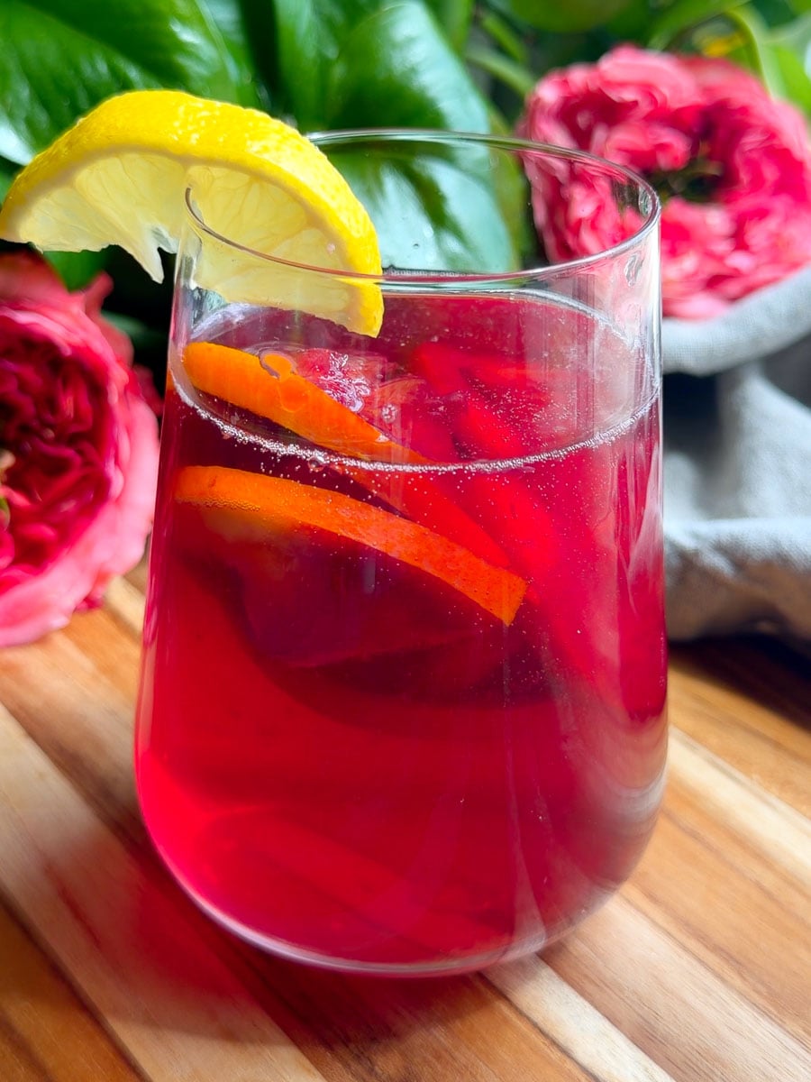 Refreshingly tinto de verano drink with citrus garnish in a glass, surrounded by pink flowers and greenery.