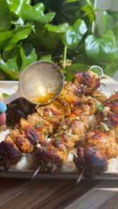 Grilled chicken skewers on rice garnished with herbs, drizzled with sauce.