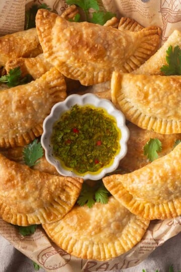 Golden fried tuna pastel with chimichurri dipping sauce and cilantro garnish.