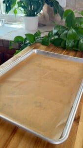 Baking tray with parchment paper on wooden counter, indoor plants in background.