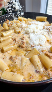Rigatoni pasta with creamy sauce, sausage, and grated Parmesan cheese in a skillet.