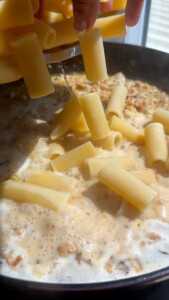 Adding rigatoni to creamy sauce in a skillet.