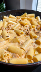 Bowl of creamy rigatoni pasta with sausage in a sunlit setting.