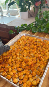 Oven-roasted seasoned potatoes on a baking sheet with greenery in the background.
