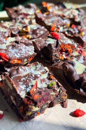 Dark chocolate tahini date bark with mixed nuts and dried berries on a wooden surface, topped with sea salt and white drizzle.