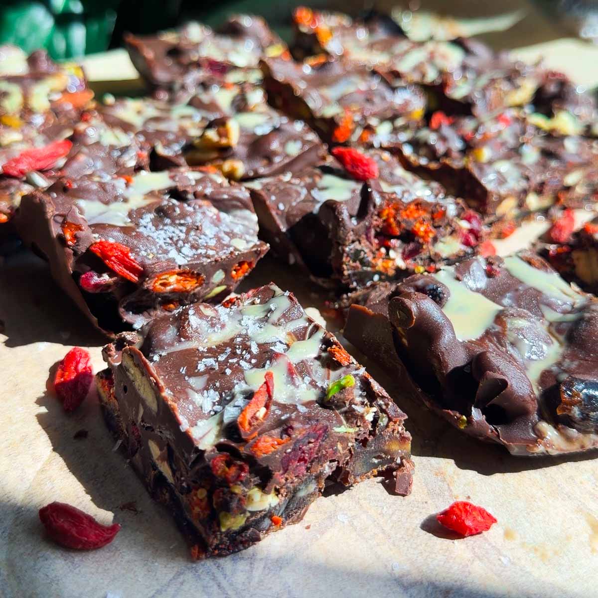 Dark chocolate tahini date bark with mixed nuts and dried berries on a wooden surface, topped with sea salt and white drizzle.