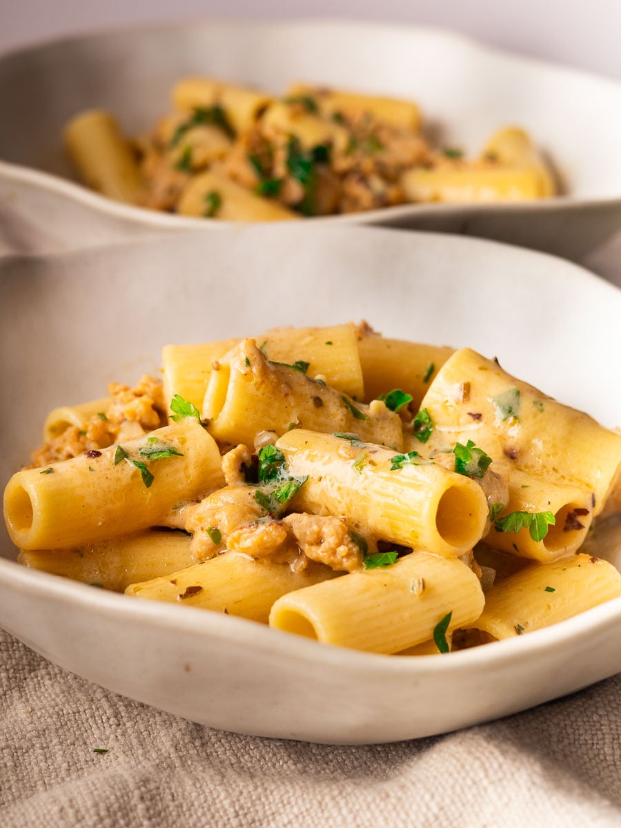 Creamy mascarpone sausage pasta with herbs and sausage in white bowls.
