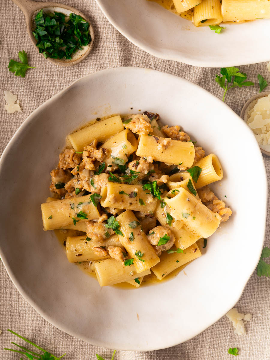 Plate of creamy mascarpone sausage pasta, garnished with parsley in a white bowl.