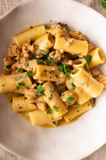 Creamy rigatoni pasta with sausage, garnished with parsley on a white plate.