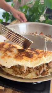 Cooking chicken stuffed quesadilla with melted cheese in a pan, spatula flipping.
