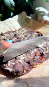 Cutting into chocolate bark with nuts and berries on parchment paper.