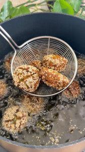 Sesame-coated falafel being deep-fried in oil in a black pot, close-up view.