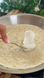 Spreading toum on a tortilla in a pan with a spoon.