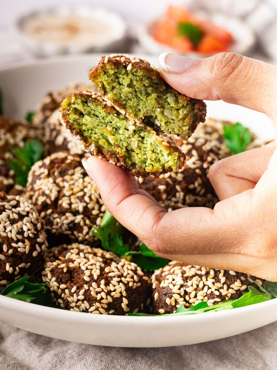 Close-up of a hand holding a halved sesame-coated homemade crispy falafel.