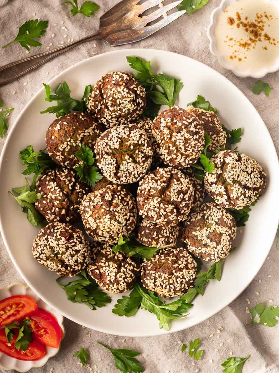 Plate of homemade crispy falafel balls with parsley garnish and dipping sauce.