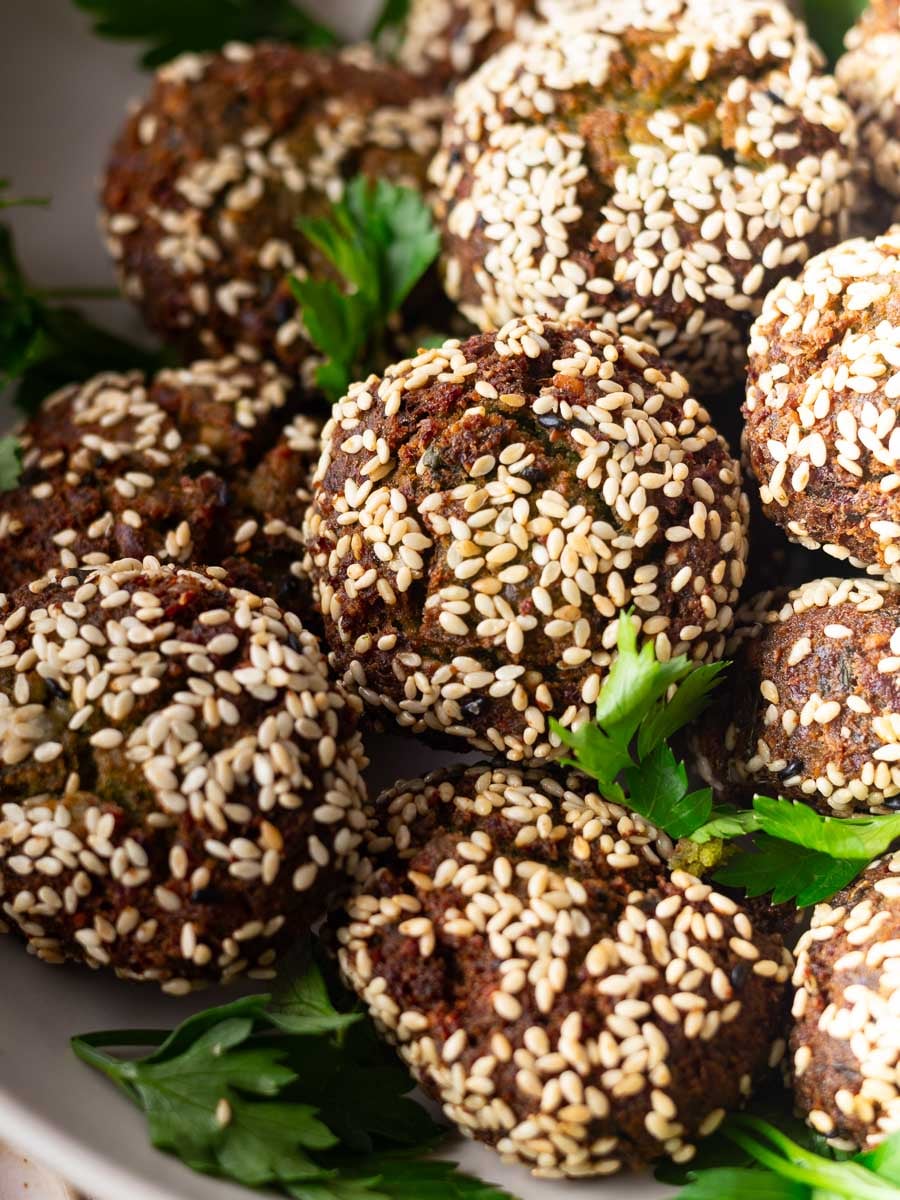 Sesame-seed covered homemade crispy falafel balls garnished with fresh parsley leaves in a bowl.