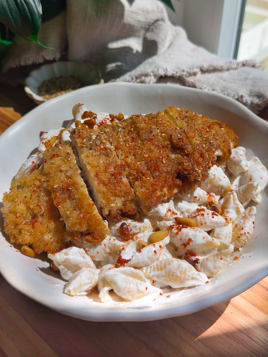 Crispy breaded chicken on creamy Lebanese Pasta in Yogurt Sauce with pine nuts and spices in a white bowl.