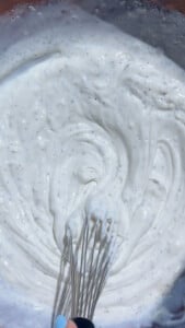 Whisk mixing creamy yogurt with black specks in a bowl.
