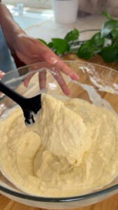 Mixing pancake batter in a glass bowl with a black spatula in a kitchen setting.
