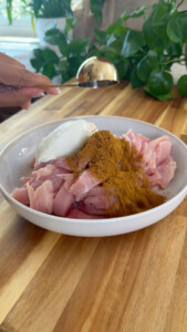 Raw chicken with yogurt and spices on a white plate on wooden table.