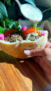 Falafel pita filled with fresh veggies, drizzled with creamy tahini sauce on wooden table.