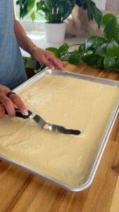 Spreading pancake batter on a baking tray with a spatula.