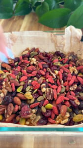Mixed nuts and dried fruits in a bowl on wooden surface.