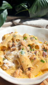 Creamy rigatoni pasta with sausage, cheese, and herbs in a white bowl, garnished with grated cheese.