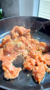 Cooking sausage chunks in a frying pan with steam rising, and a wooden spatula stirring.