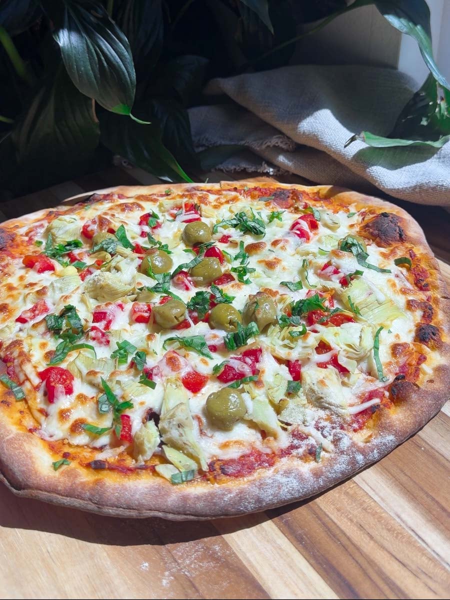Homemade freezer pizza with olives, artichokes, and bell peppers on wooden table.