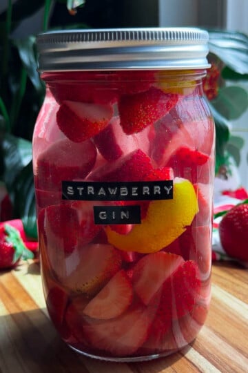 Jar of homemade strawberry gin with lemon slices on a wooden table.