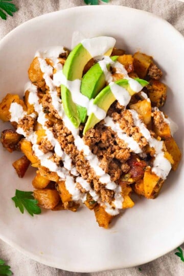 Lebanese potato bowl with seasoned potatoes, ground meat, avocado, and drizzled yogurt sauce.