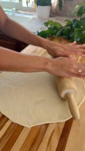 Rolling out pizza dough on wooden countertop with rolling pin.
