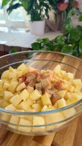 Diced potatoes with spices in a glass bowl, ready for cooking in a cozy kitchen setting.