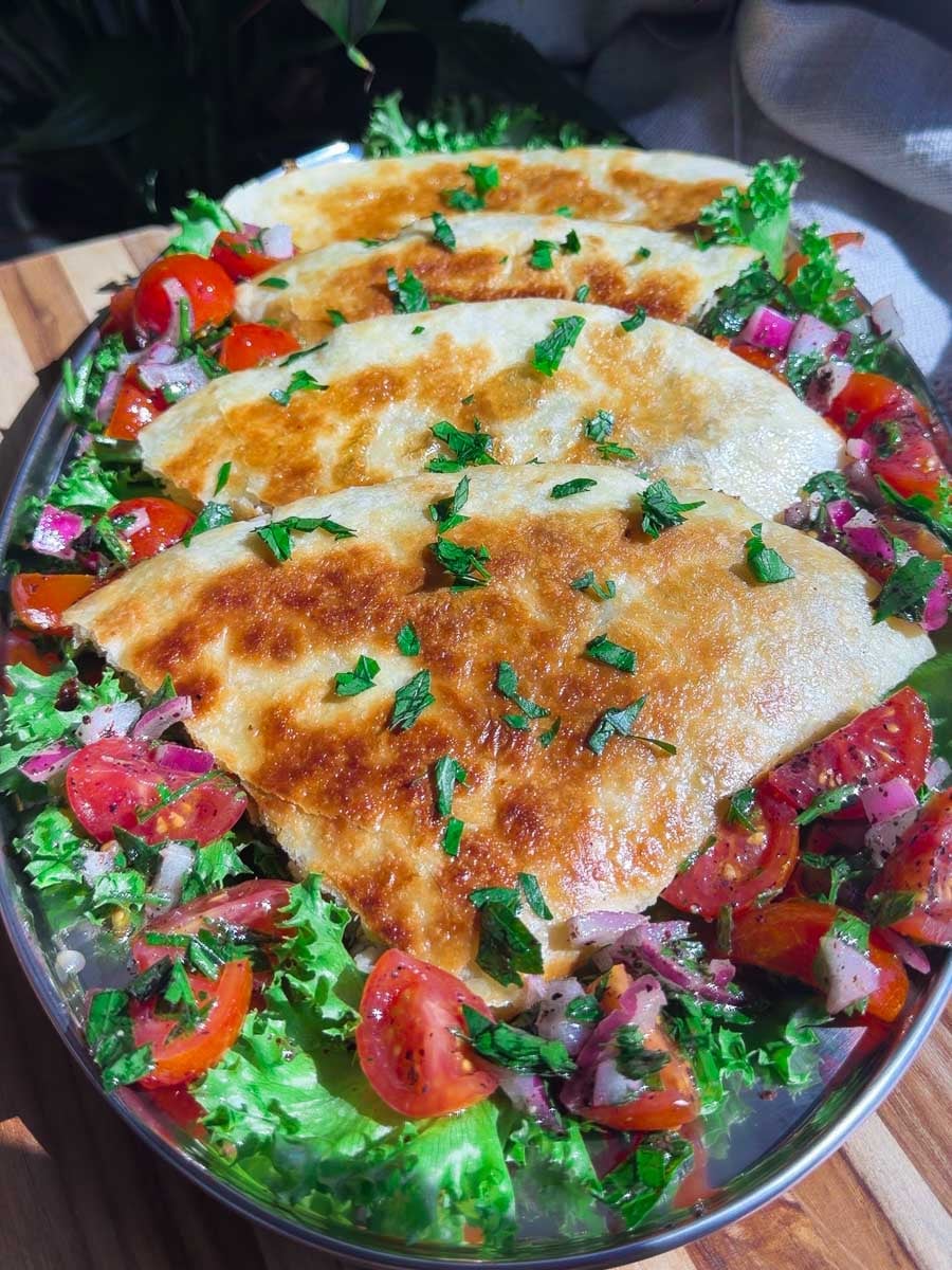 Shawarma quesadilla with fresh salad, tomatoes, and onions on a platter.