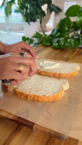 Spreading aioli on fresh sourdough bread slices in a kitchen setting with plants.