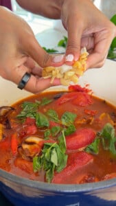 Adding fresh garlic to a pot of tomato basil soup in a blue enamel pot.
