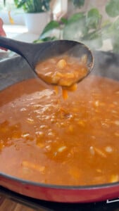 Brava sauce being stirred in a pot with ladle, steam rising.
