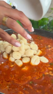 Hand adding gnocchi to simmering tomato sauce in a pan.