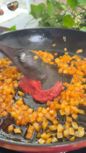 Cooking diced onions and tomato paste in a pan with a wooden spoon.