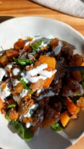 Forkful batata brava with spinach and creamy topping.