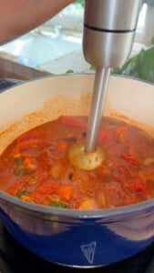 Blending tomato soup in a blue pot with an immersion blender.