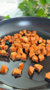Diced chorizo cooking in a non-stick pan with a green plant background.