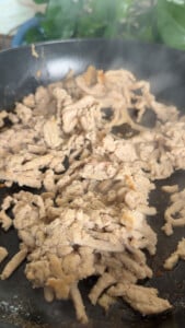 Sizzling ground chicken cooking in a black skillet with steam rising.