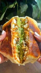 Hands holding a crunch wrap filled with chicken, falafel and lettuce.