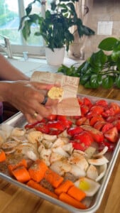 Preparing seasoned vegetables with spices and garlic for roasting on a sheet pan in a bright kitchen.