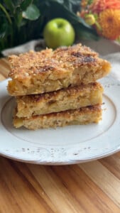 Three slices of apple pie crumble pancakes stacked on a decorative white plate.