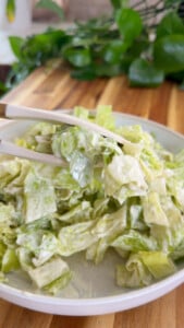 Fresh Caesar salad with creamy dressing being served from a white bowl on a wooden table.